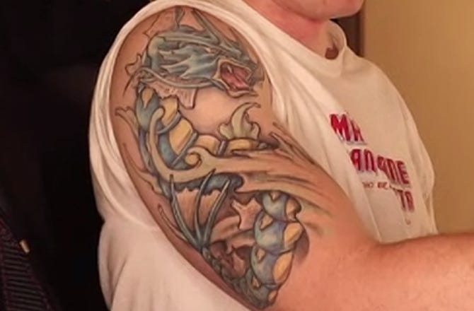 Photo of a man's upper right arm. On his arm is a large tattoo of a blue, serpentine Pokemon