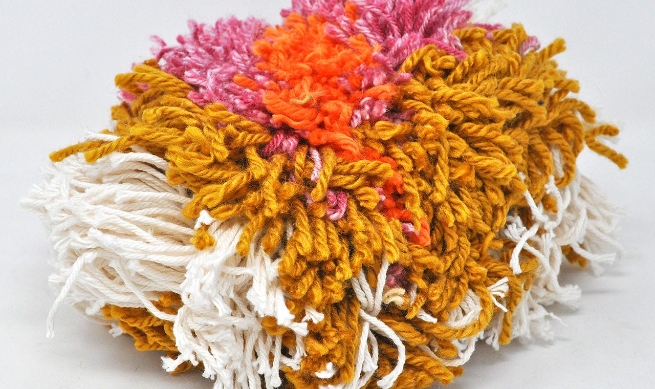 Installation view of a pom-pom made of multi-colored yarn.