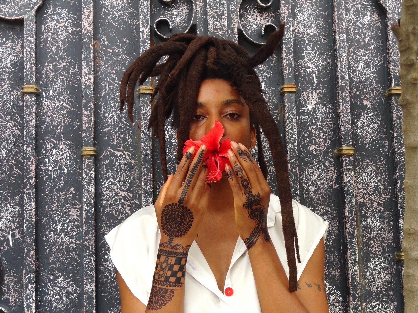 N3VLYNNN holds a red hibiscus flower in front of her mouth with henna painted hands