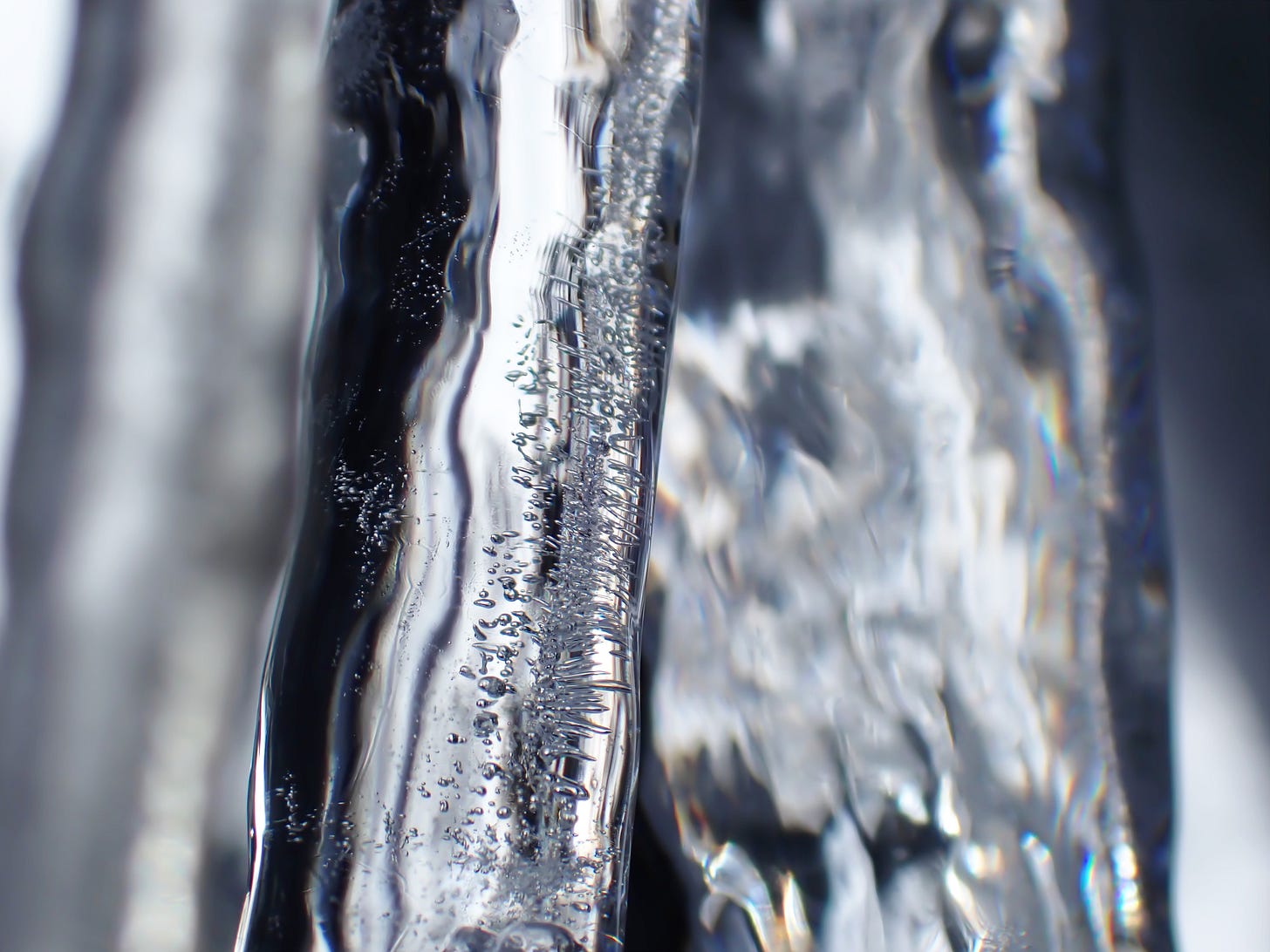 A close-up of clear icicles, with trapped air bubbles and wavy forest reflections.