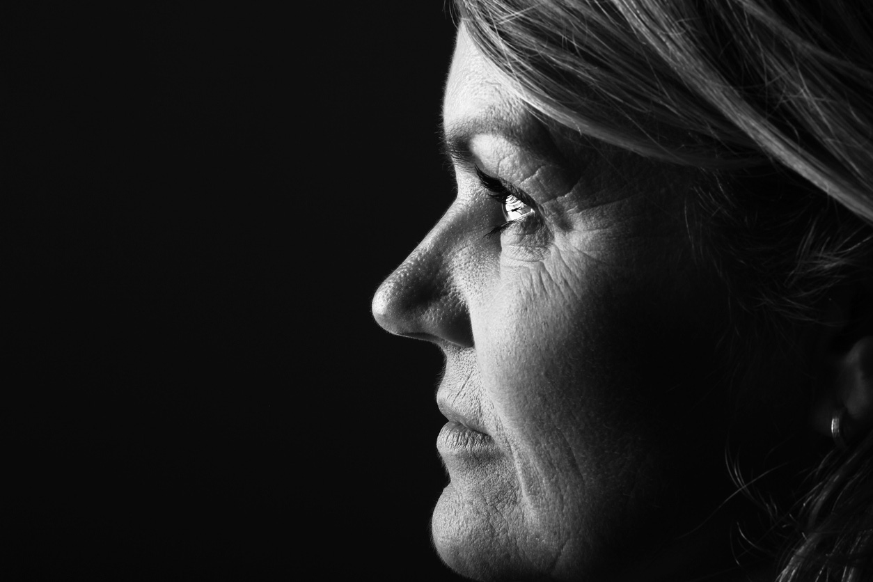 Black and white tight shot of older white woman as a profile against a black background.