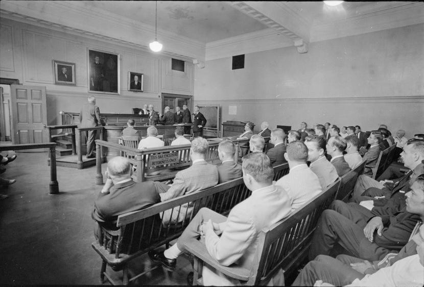 Black-and-white photo showing the inside of a courtroom. The photo was taken on July 23, 1963 and depicts "Judge Adlow presiding over a session in Boston Municipal Courtroom where new police officers are observing," according to Digital Commonwealth.