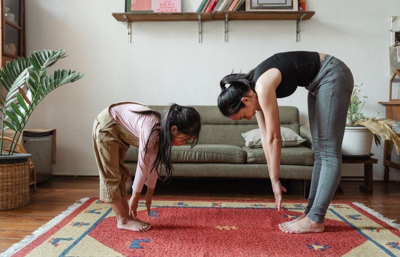 A child and an adult, both standing bent over, stretching towards their feet