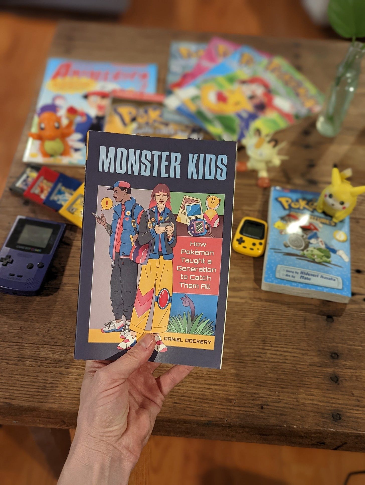 A photograph from Daniel with his copy of Monster Kids, surrounded by some of his Pokémon belongings. The book is available in paperback, eBook, and audiobook