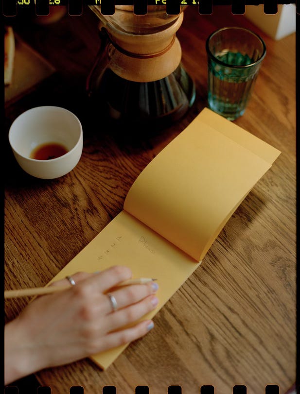 a hand with a pencil writing on a yellow pad on a wooden table