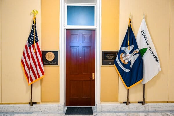 The doorway to the office of Mike Johnson, the speaker of the House, with three flags displayed outside: the American flag, the Louisiana flag and an “Appeal to Heaven” flag.