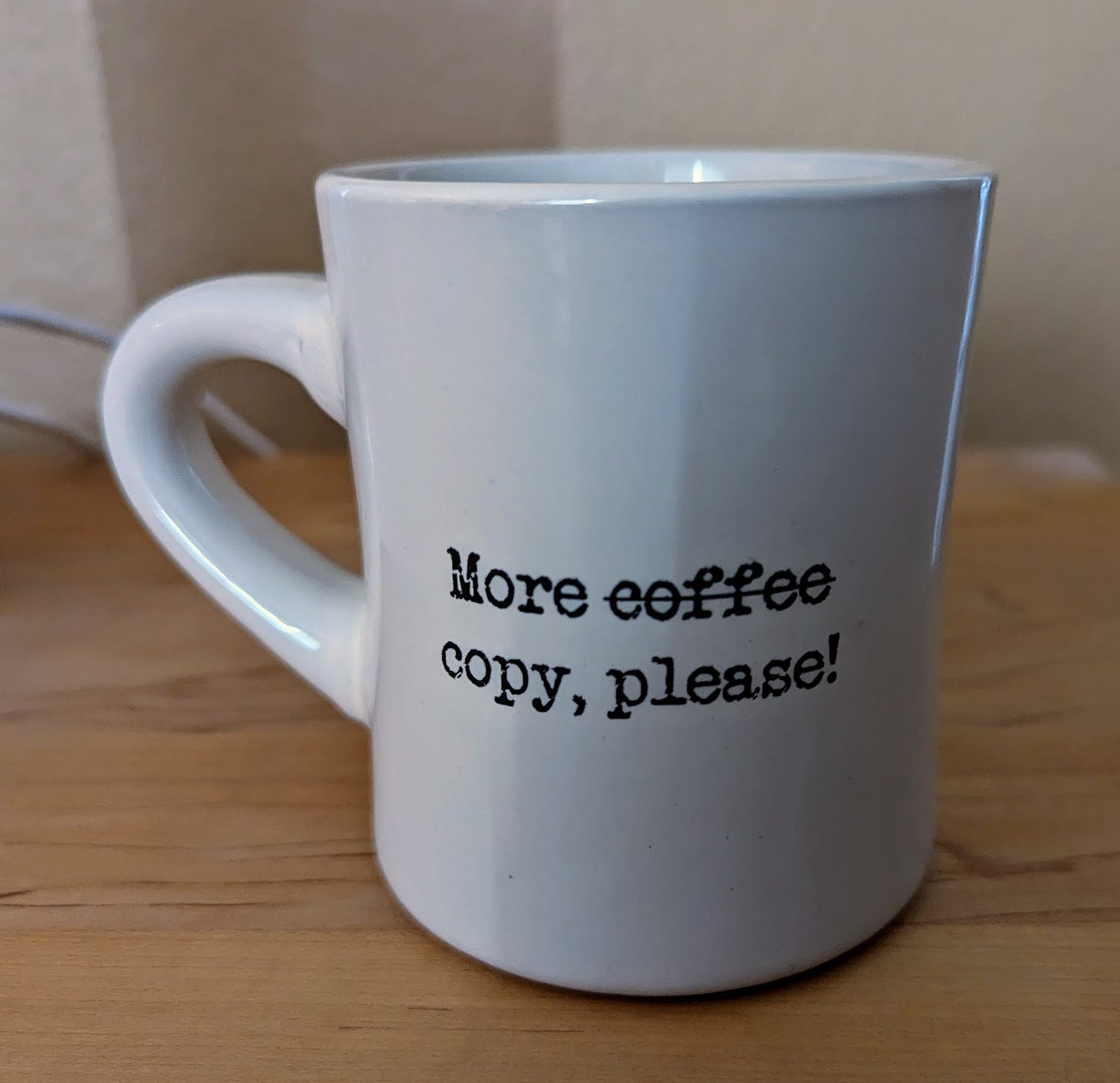 White coffee mug with black lettering that reads "More coffee please"; "coffee" is replaced with "copy"