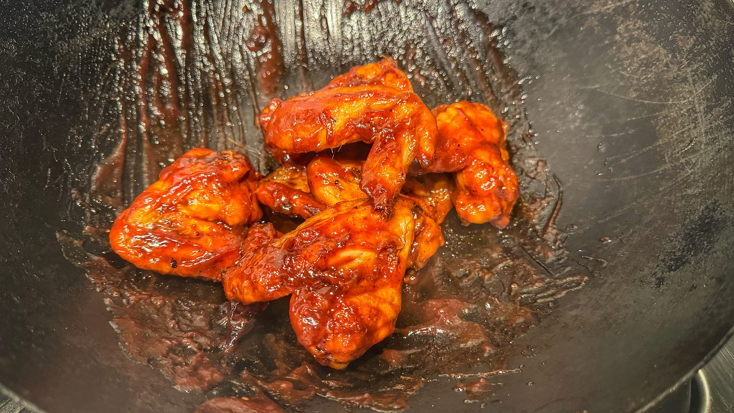 Cooked wings coated in Mumbo sauce being tossed in a hot wok