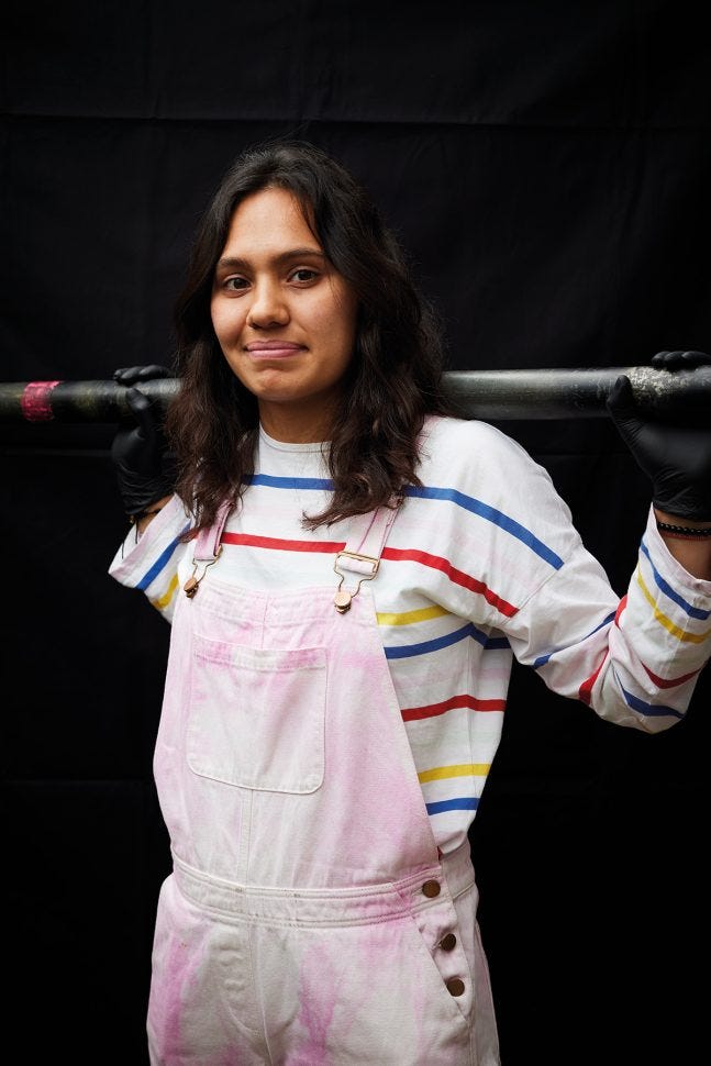 Silvi is wearing white overalls and holding a scaffolding pole