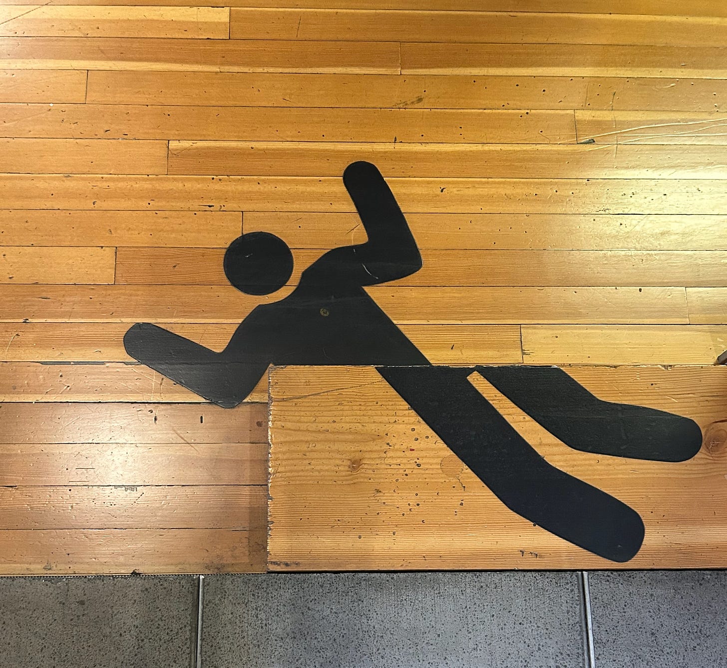 A photo of a hardwood floor and an abrupt step, with a large warning graphic of a stick man falling off the edge