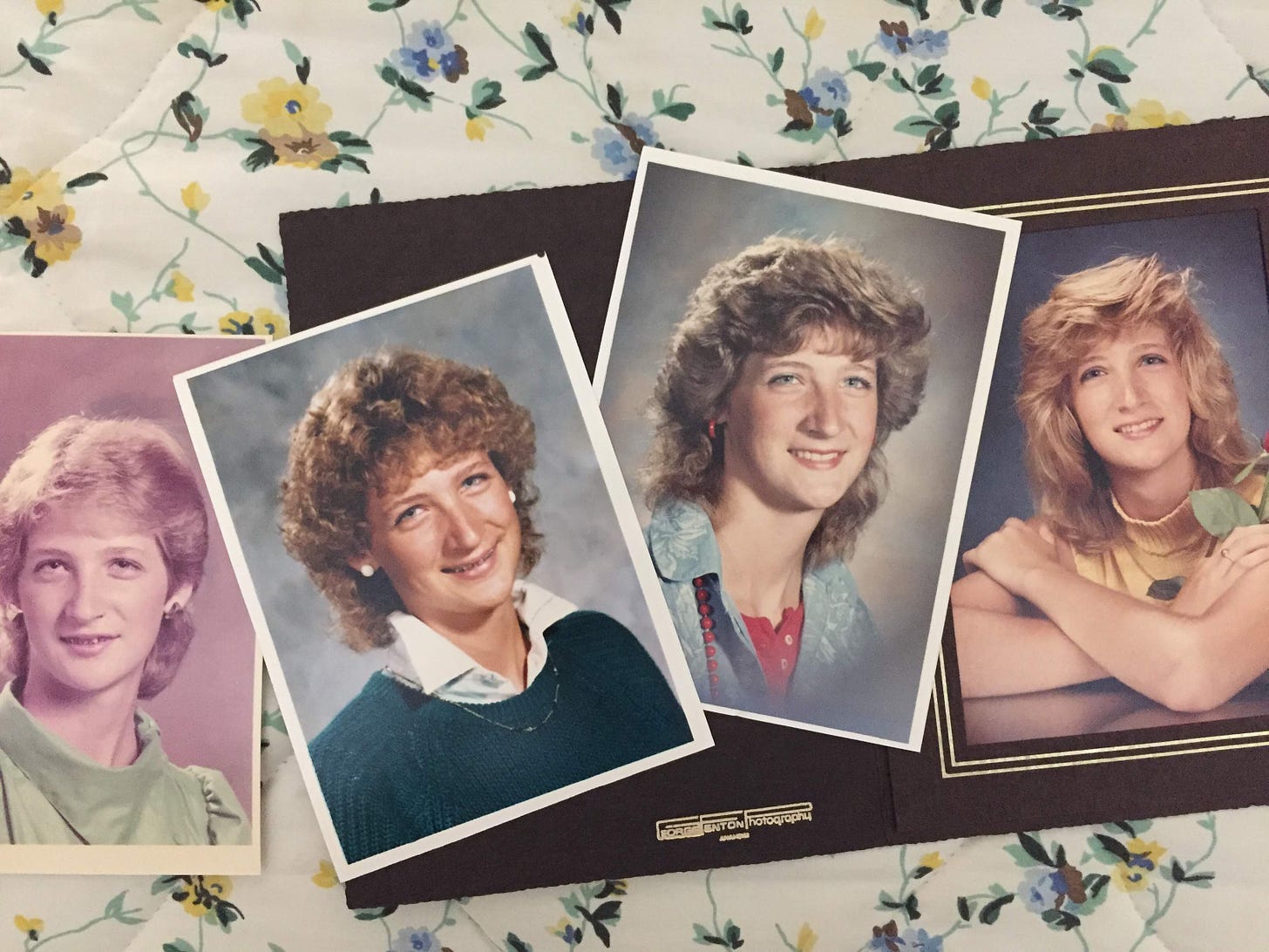 Four school photographs spread out on a flowered bedspread, one for each year of highschool, all looking like the 1980s