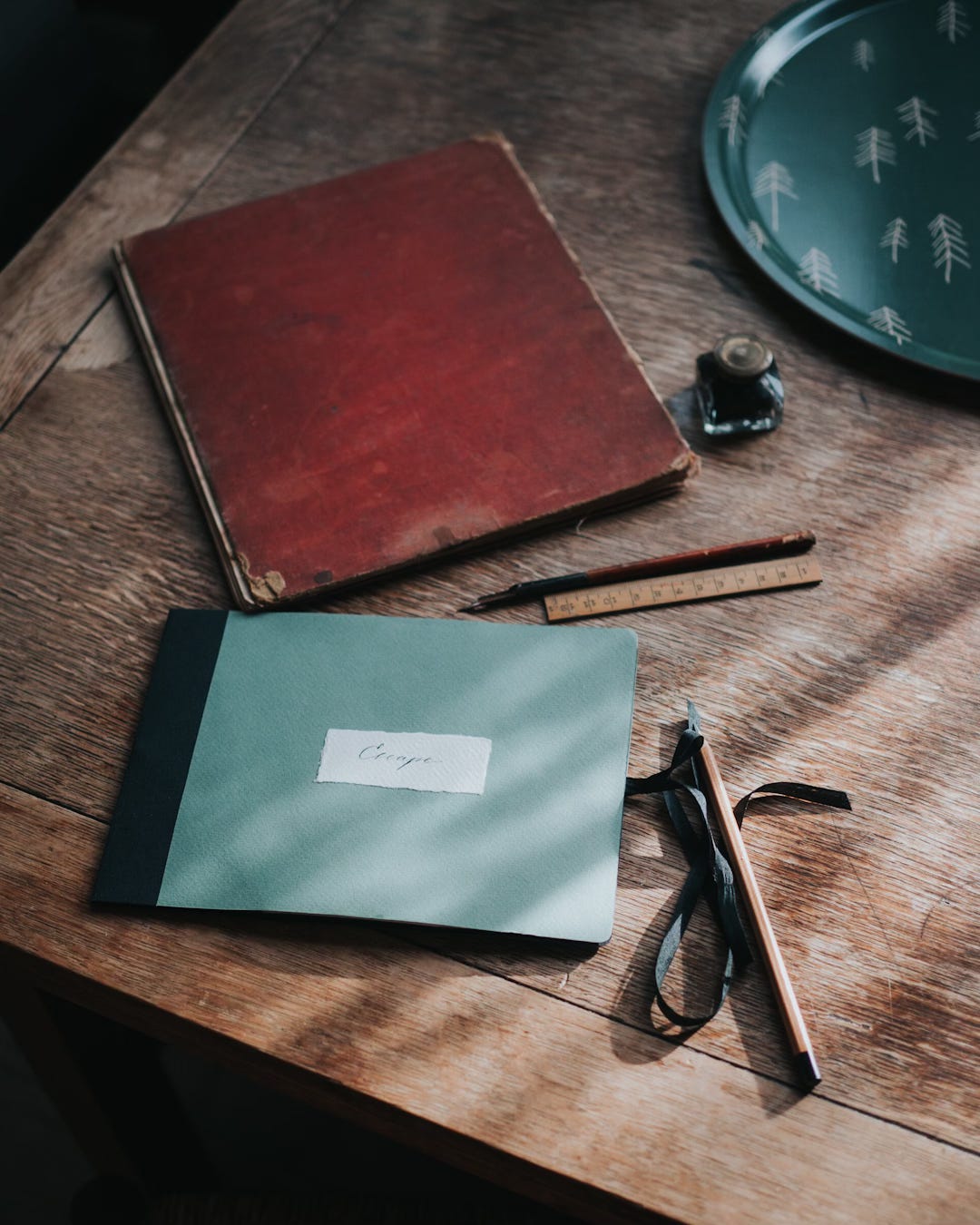 A bound map with a green cover and the title ‘escape’ in calligraphy, pens, and ink bottle, a green tray and a dark red book on a wooden table