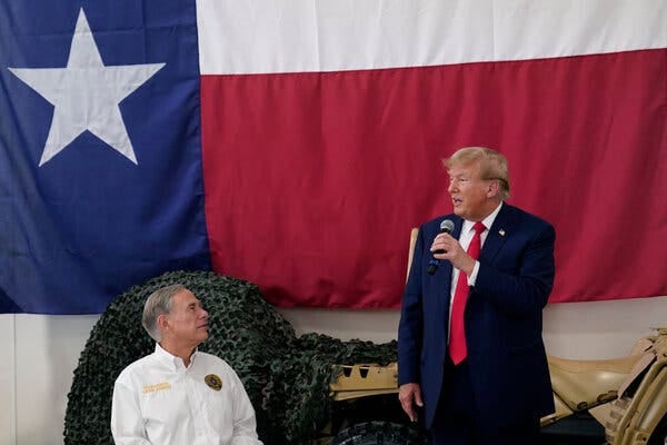 Gov. Greg Abbott of Texas, seated at left, looks toward Donald Trump, who is standing and holding a microphone with his left hand. A large Texas flag is hanging behind them.