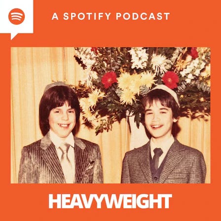 Artwork van de aflevering. Tegen een oranje achtergond zie je een jeugdfoto waar Lenny en Jonathan op staan, in pak voor een kerstboom. De twee witte jongetjes zijn een jaar of tien, hebben halflang zwart haar en lachen. Onder de foto staat de titel HEAVYWEIGHT in wit, bovenaan het logo van Spotify en de tekst ‘A Spotify podcast’.