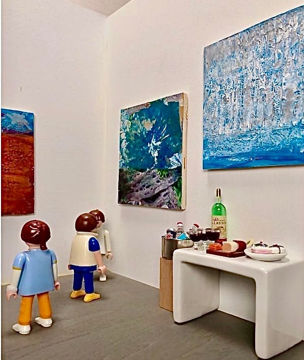 Pieces of art in a micro gallery and little figures as well as a tiny table with wine and nibbles like any other gallery. One piece resembles a bright blue and white starburst coming out weathered wood with large holes. The second piece is a row of silves birches on a blue textured background.