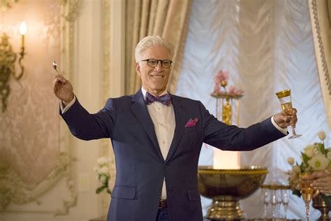 Ted Danson, in a blue suit, smiling , with both hands wide with a glass a spoon in each hand about to make a toast.