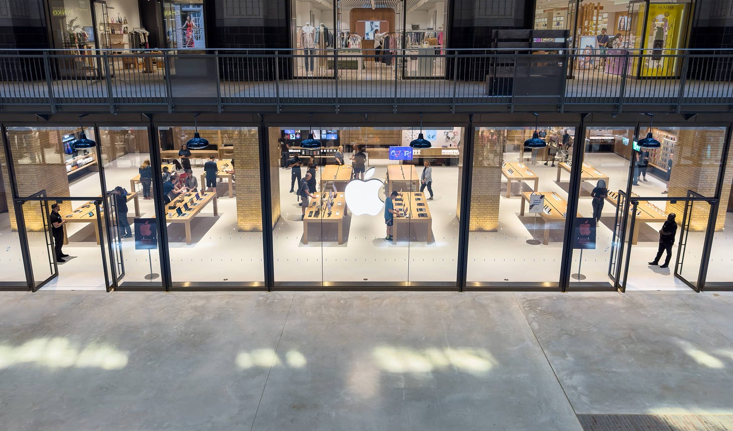 The storefront of Apple Battersea from an upper balcony. Customers move about the tables inside.