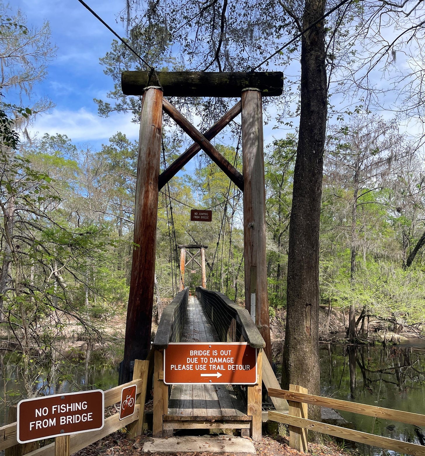 Suspension bridge across a river. Signs on bridge indicate it is out of order. 