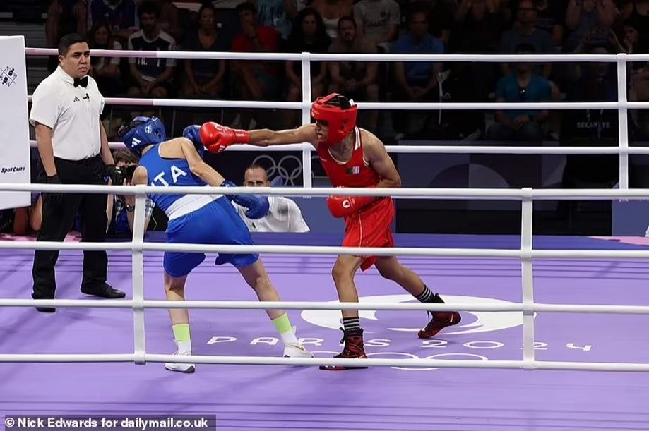 Imane Khelif, dressed in red, extends his arm to maintain distance from his opponent in blue, who ducks to avoid his powerful male punch from connecting in what could be a deadly blow at any moment. This scene highlights the controversial physical disparities in a match, questioning the integrity of gender divisions in sports.