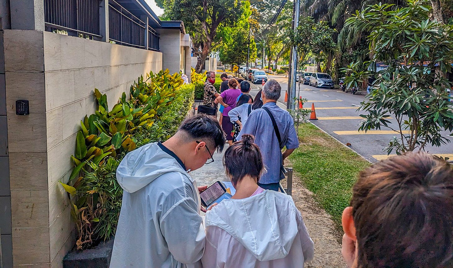 People lined up on a green, tree-lined street outside the Thai consulate in Penang, Malaysia. 