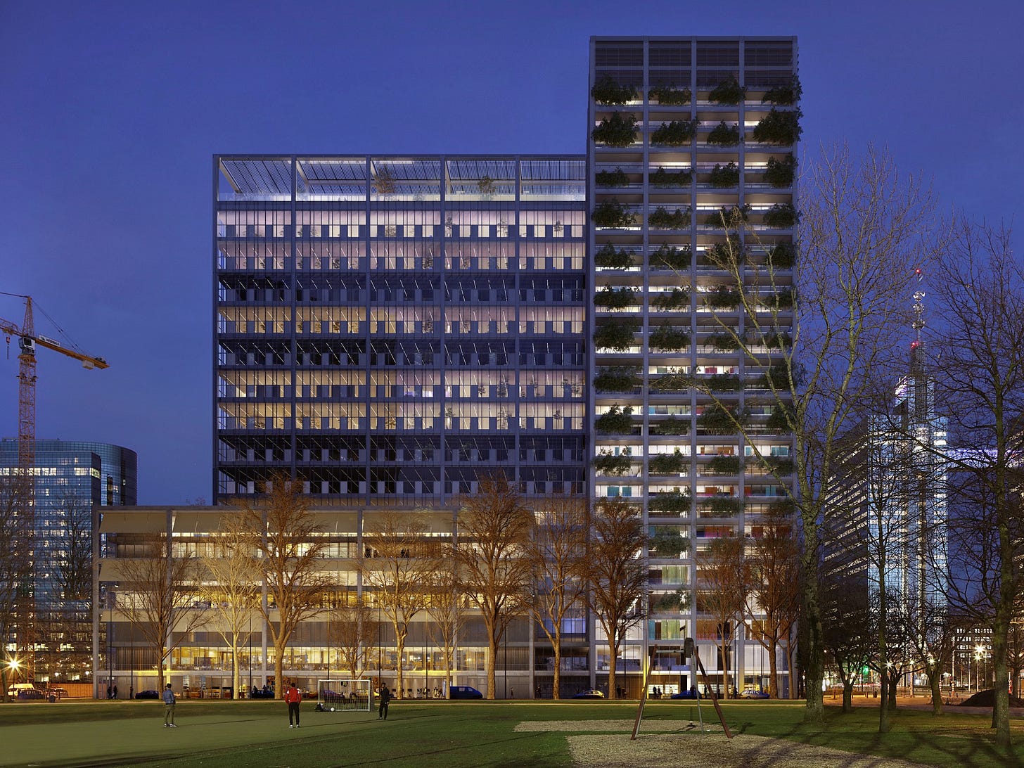 Photo, taken at night, of a multi-part mid-rise office tower in Brussels, with a park in the foreground and other buildings in the background