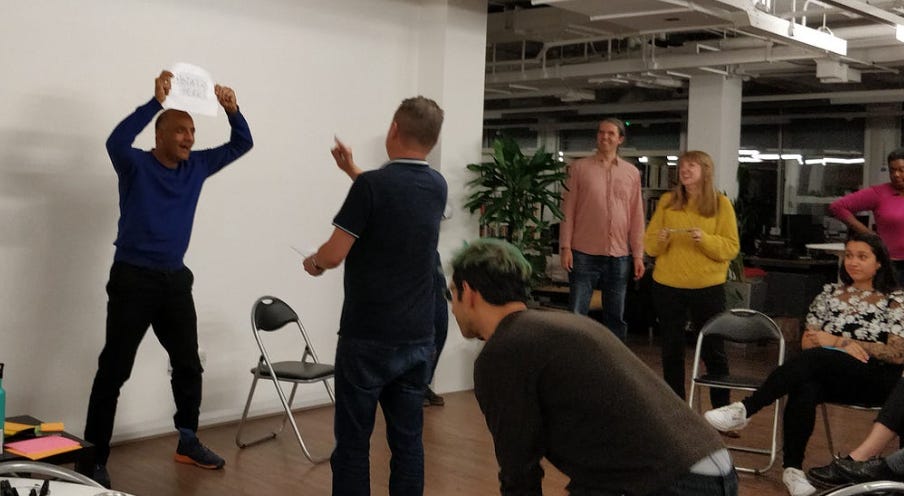 A group of people watching a man reenact a user problem scene with another man directing. 