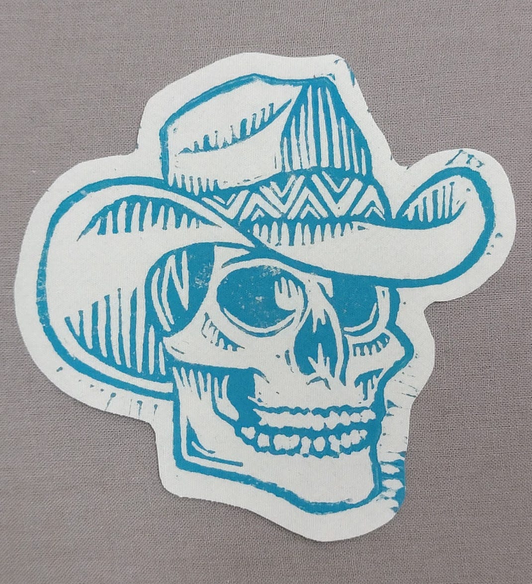 Teal linocut print of a skull wearing a cowboy hat.