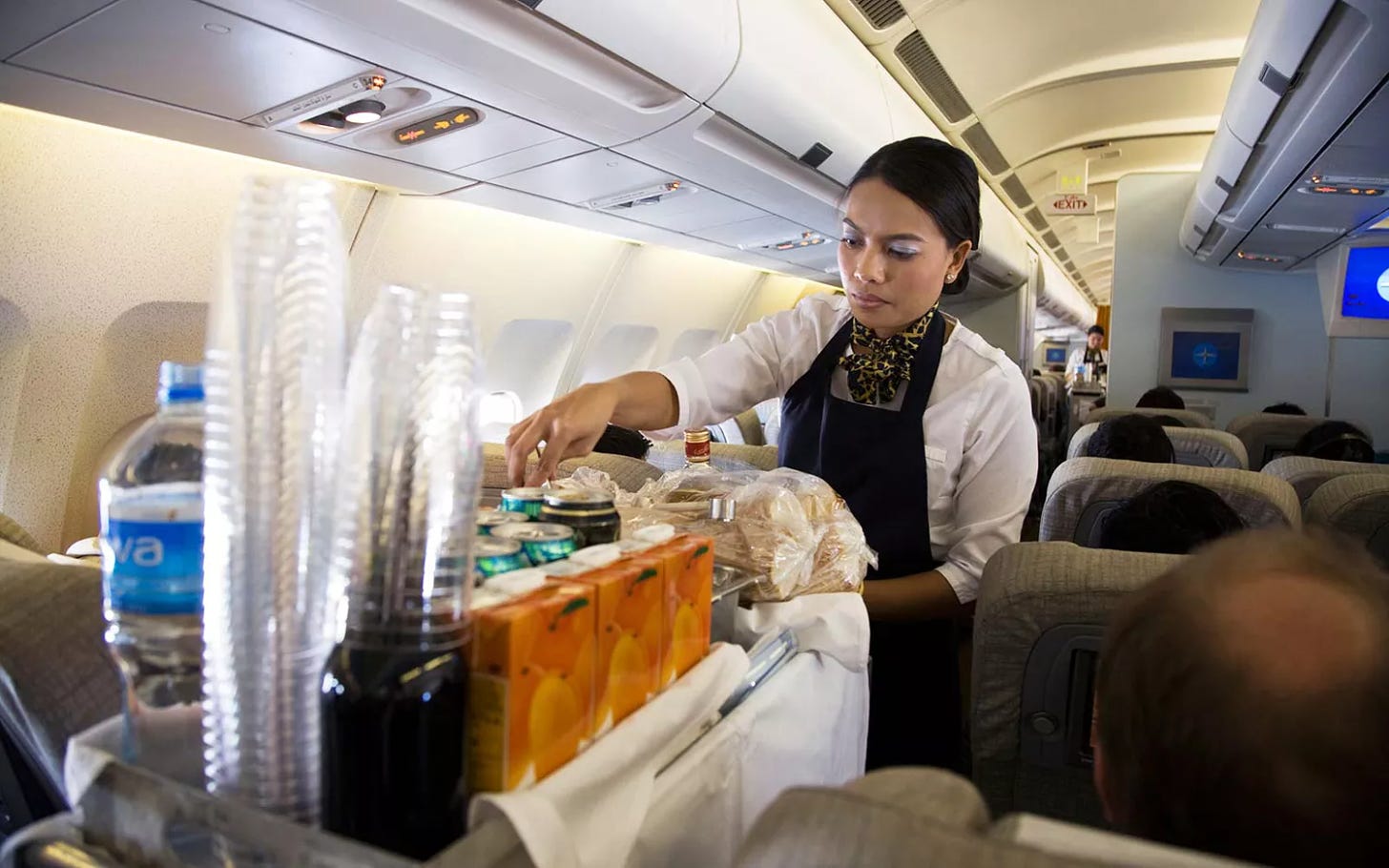 Cabin crew / air stewardess serves drinks to passengers from a beverage cart during a flight