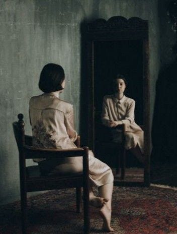 This may contain: a woman sitting in a chair looking at herself in the mirror with another person standing behind her