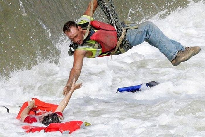 Image of a man suspended over a waterfall reaching out his hand to save a drowning person.