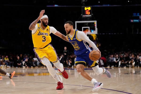 Golden State’s Stephen Curry dribbles past the Lakers’ Anthony Davis, who is running alongside Curry.