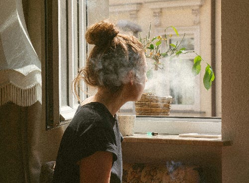 woman sitting by a window with a cloud of smoke in her face. Wildfires woman sitting by a window with a cloud of smoke in her face. Wildfires