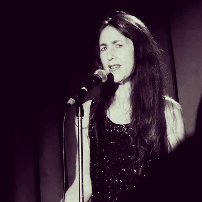 Black and white photo of Jan singing at a microphone. Her expression is passionate, and her dress is sparkly.