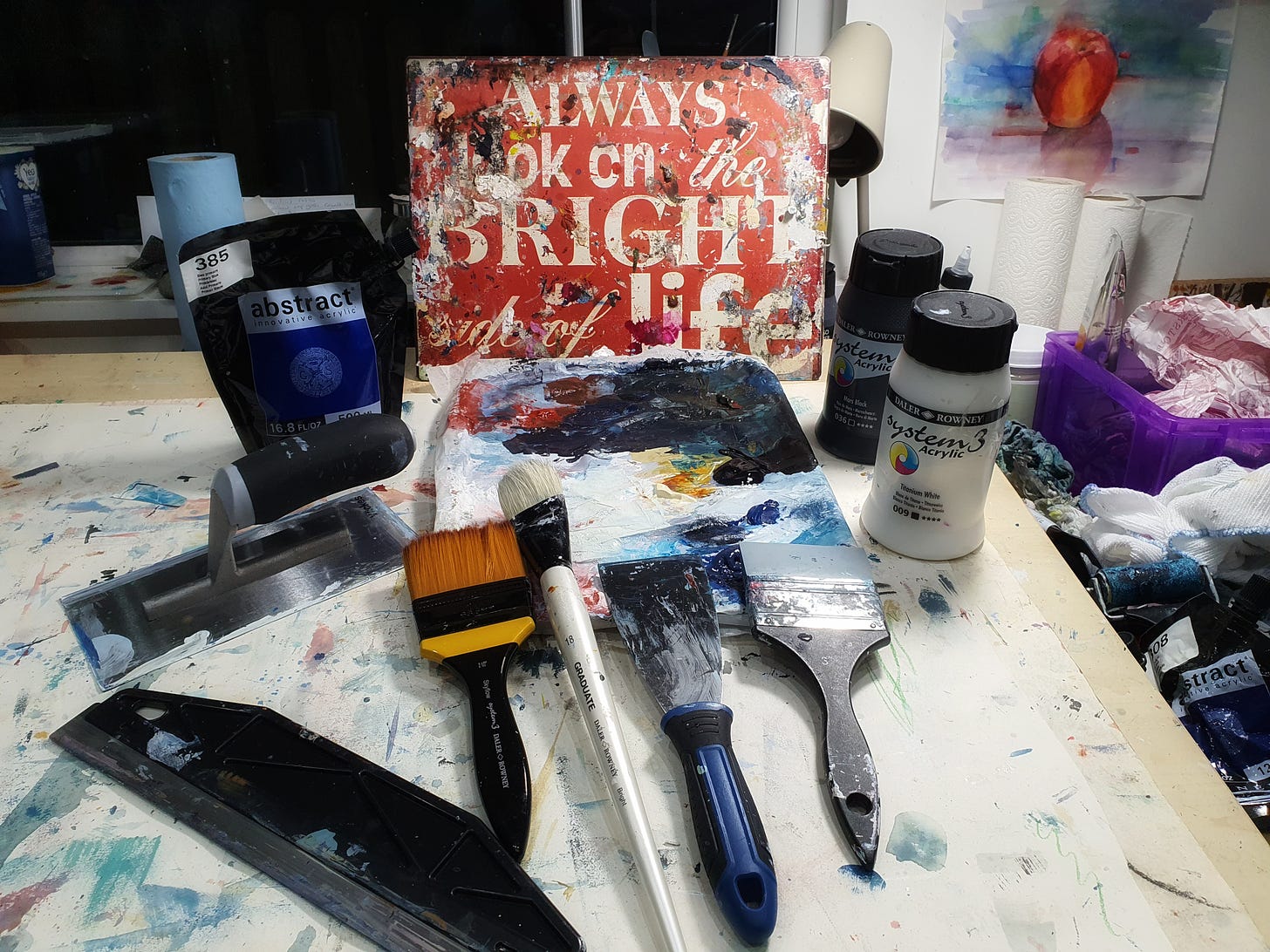 image shows susan mills studio with a selection of painting tools and paint and a sign that says Always look on the bright side of life