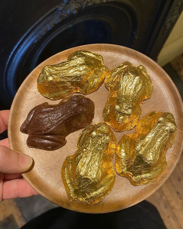 A wooden plate with five gold-foiled chocolate caramel frogs on it.