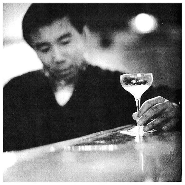 A blurred black and white image of a man, Haruki Murakami, holding a cocktail glass in one hand.