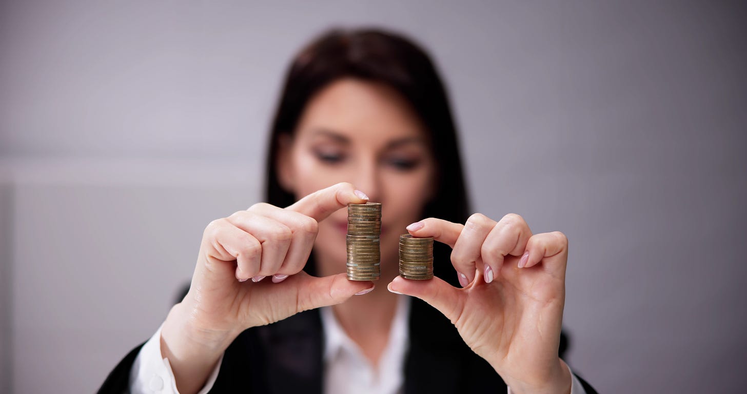 Young businesswoman dressed in a suit contemplates two stacks of coins that are different heights