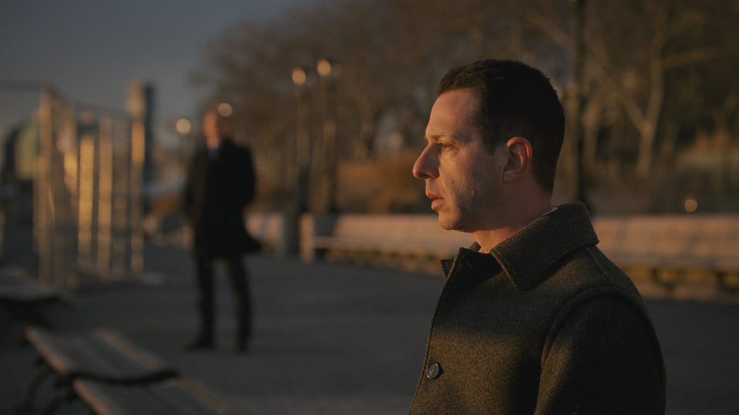 Kendall staring out at the river during the last episode of Succession; Colin the bodyguard looks on.