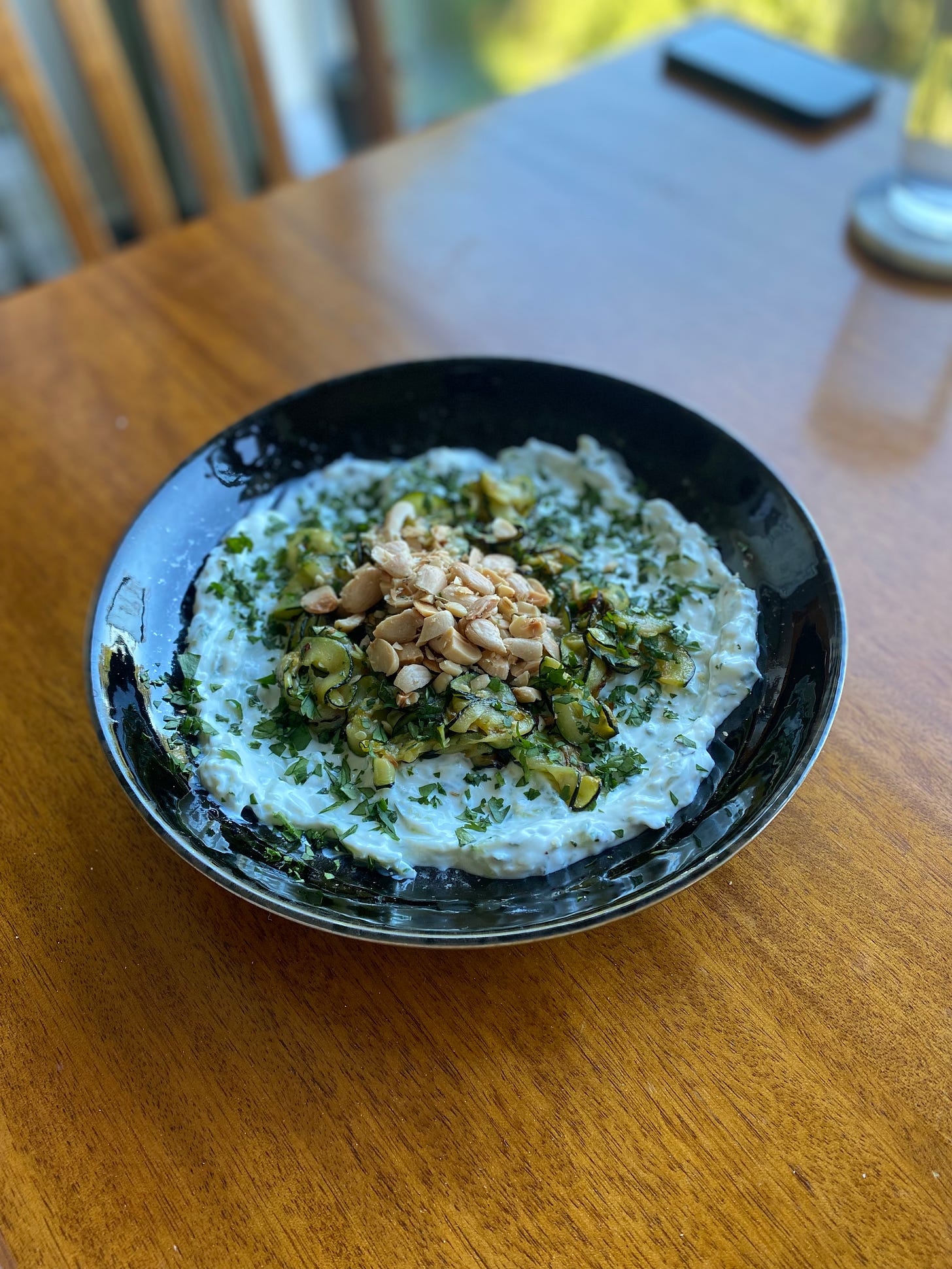 A black dish with a base layer of tzatziki, topped with a pile of thin zucchini slices and chopped Marcona almonds. Everything is dusted with a mix of parsley, mint, and cilantro.