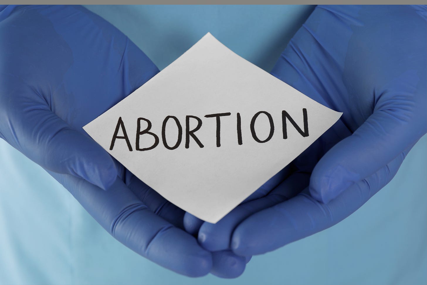 hands with surgical gloves holding sign that says "abortion"