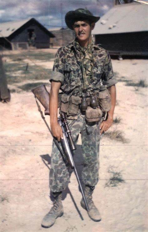 Mawhinny stands in Vietnam. He is wearing camouflage and holding his rifle.