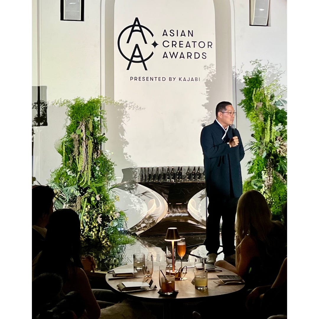 Jerry Won on stage speaking to an audience. Behind him a sign on the wall reads: Asian Creator Awards presented by Kajabi