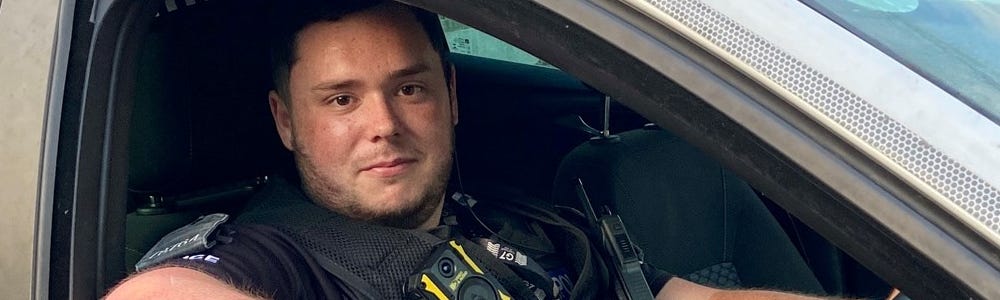 PC Luke Edmonds sitting in a police car with his elbow resting on the open window ledge