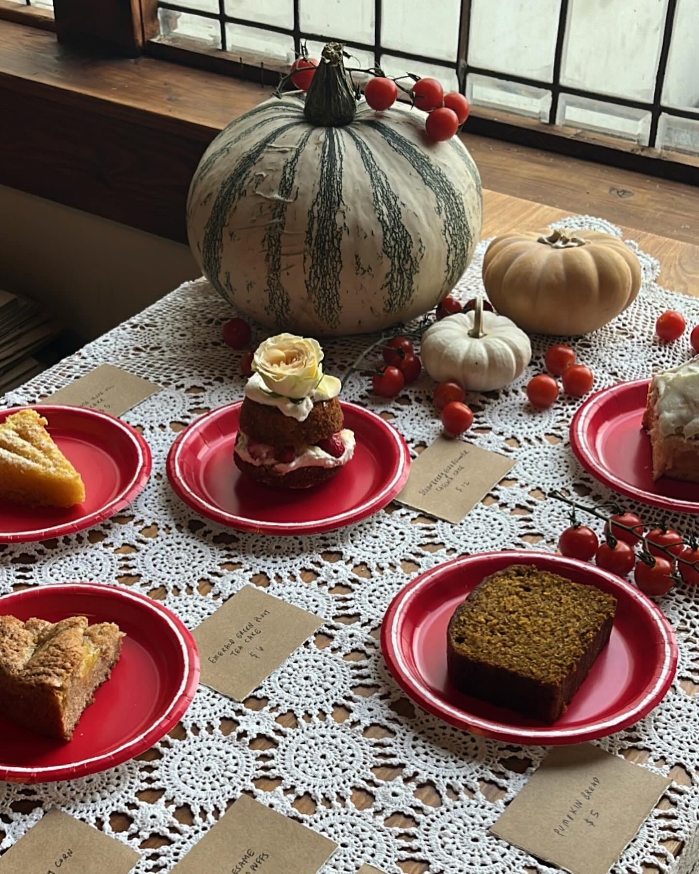 Image of a variety of pastries spread out on a lace doily tablecloth. Decor of pumpkins and cherry tomatoes strewn throughout.
