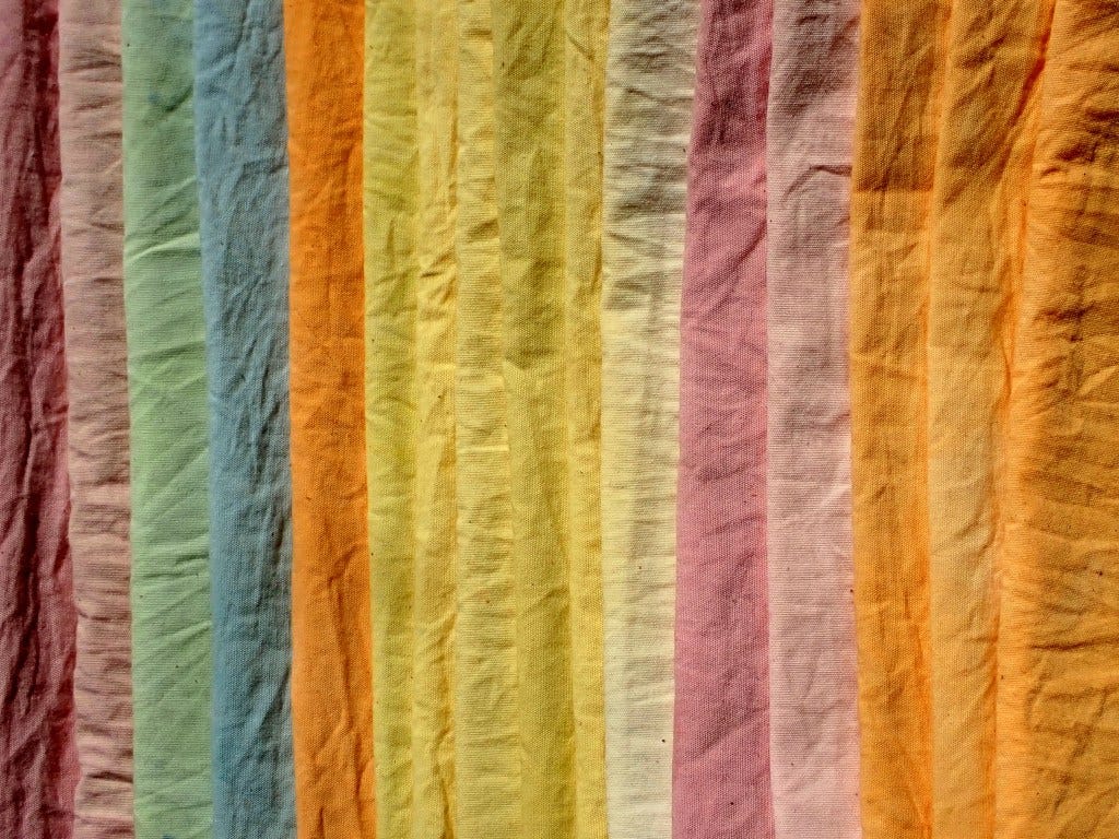 An array of wildflower-dyed muslin, in pink, orange, yellow, blue and green, is stacked in the sunshine.