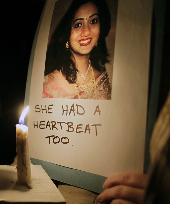 Picture of Savita Halappanavar in Ireland with the words: She had a heartbeat too.” Savita died of sepsis after being denied an abortion on the grounds that the fetus she was miscarrying still had a detectable heartbeat