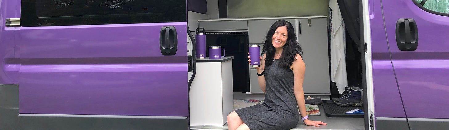 Woman in a gray dress sitting in the open door of a purple van, holding a purple YEI coffee thermos.
