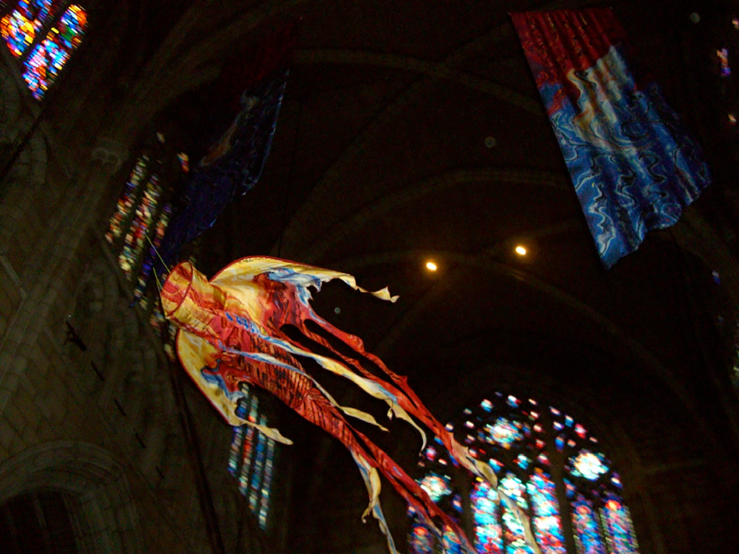 a colorful liturgical kite flies through the air inside a dim church with stained glass in the background