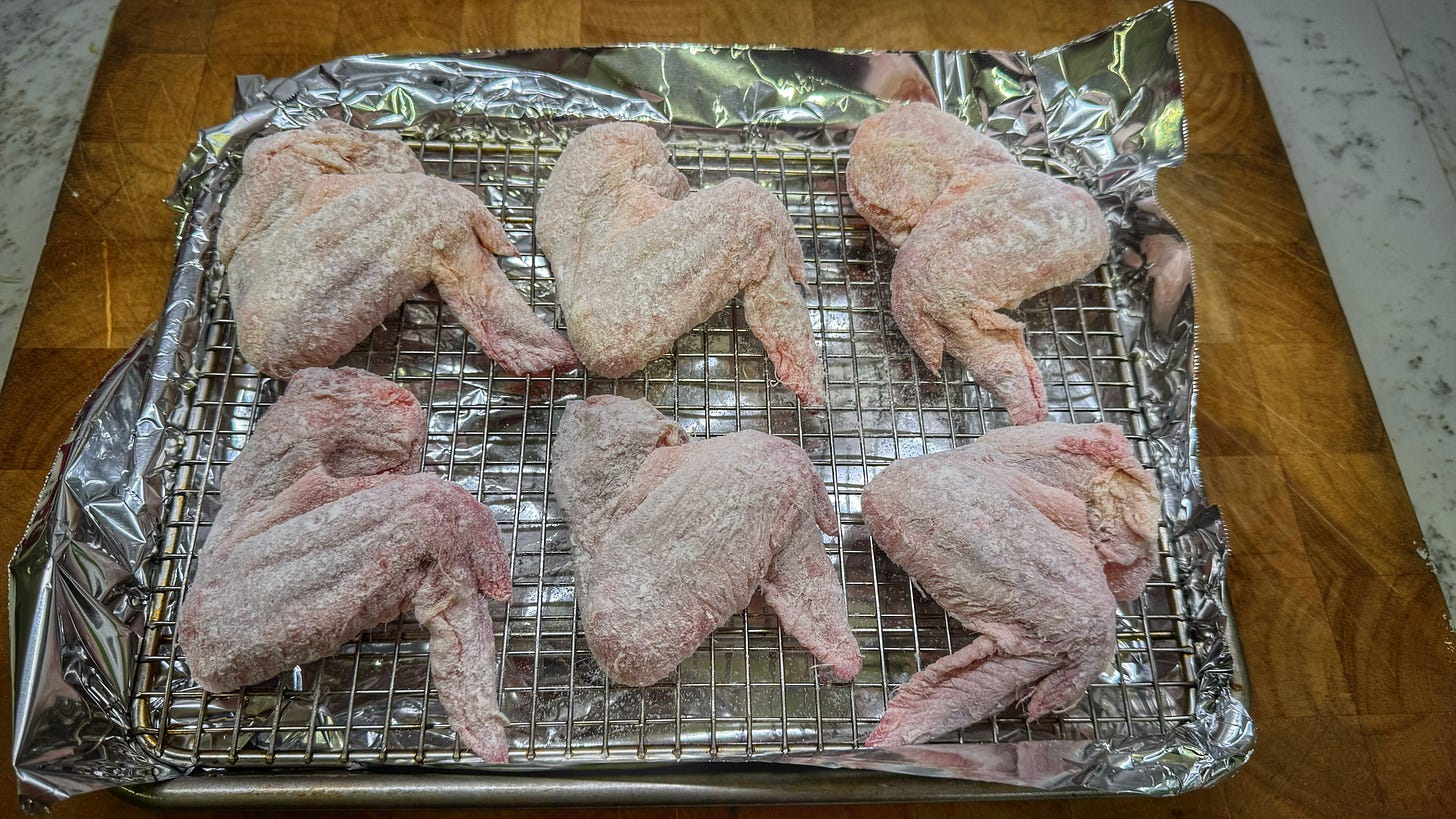 Uncooked whole chicken wings on a rack over a baking sheet covered in aluminum foil. The wings have been dusted in rice flour, corn starch, and baking powder