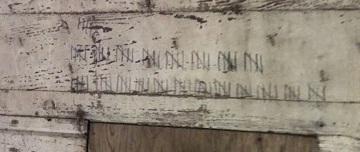 Two rows of tally marks on a rotting white wall. There are 104 marks in total.